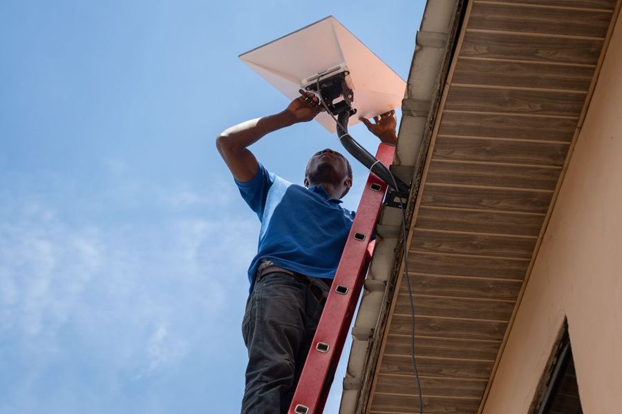 Technician on a ladder installing a Starlink dish on a building